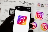A silhouetted hand holding an iPhone with the Instagram logo on it