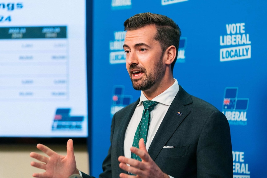 A man standing at a lectern with his hands in front of him.