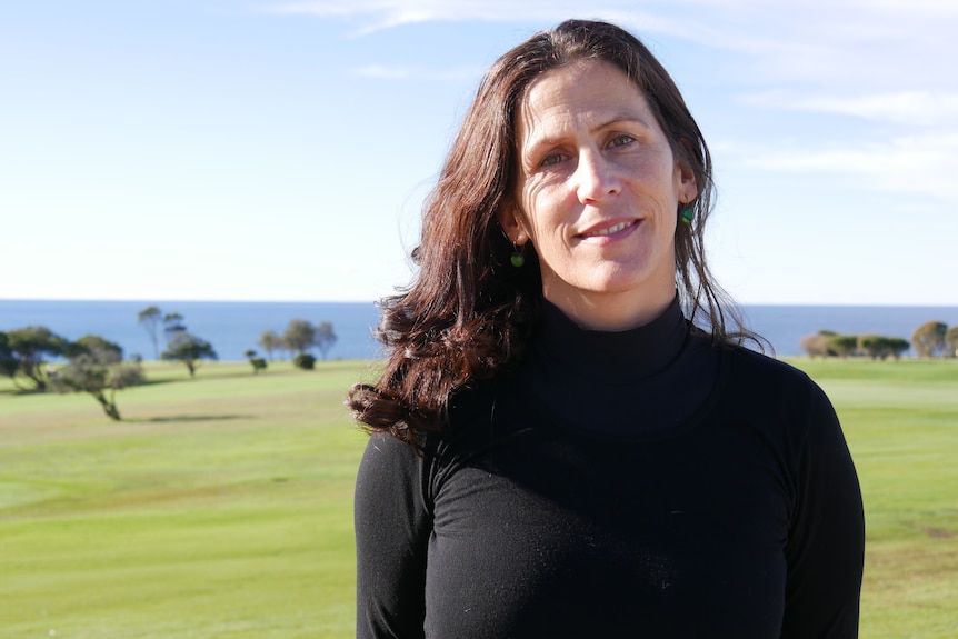 A woman in a black shirt smiling at the camera in front of a golf course.