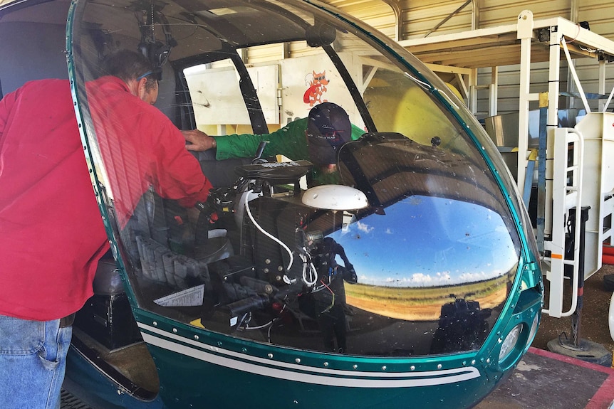 A pilot and mechanic work to repair a helicopter in a shed