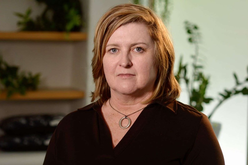 Angela Lynch with shoulder length red hair wearing a maroon shirt sits in her office.