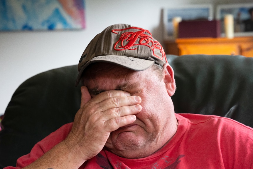 A middle-aged man covers his face as he sits in a room crying.
