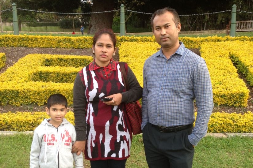 A Bangladeshi family of a mum, dad and son stand in a garden.