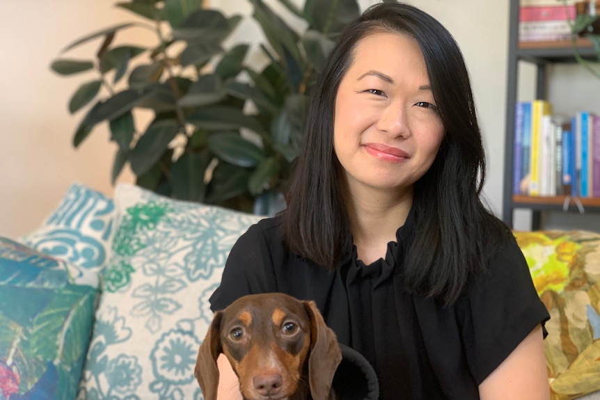 Young Asian woman sits on couch with small dog.