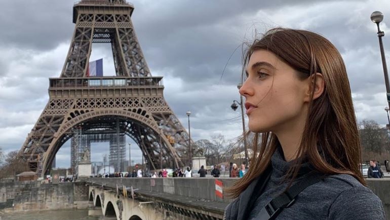 A girl stands in front of the Eiffel Tower and looks into the distance