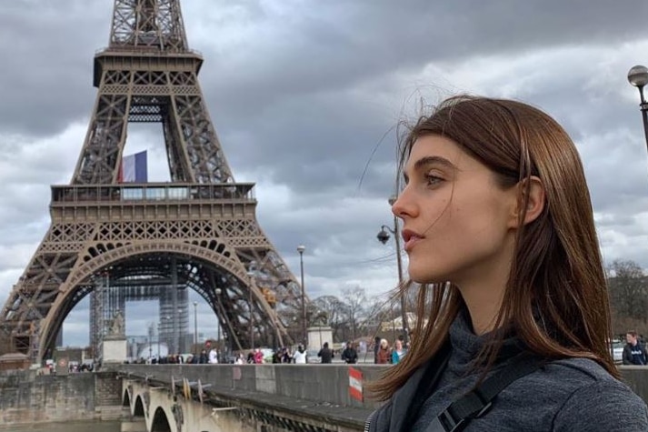 A girl stands in front of the Eiffel Tower and looks into the distance