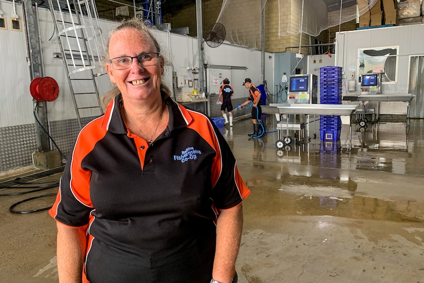A woman wearing an orange and black shirt standing in a seafood processing centre.