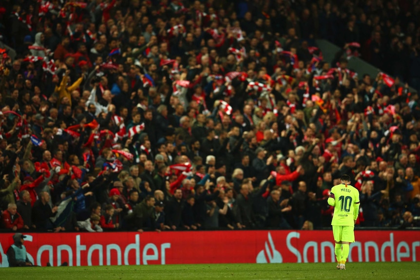 A football player looks down to the ground as fans in the stand celebrate