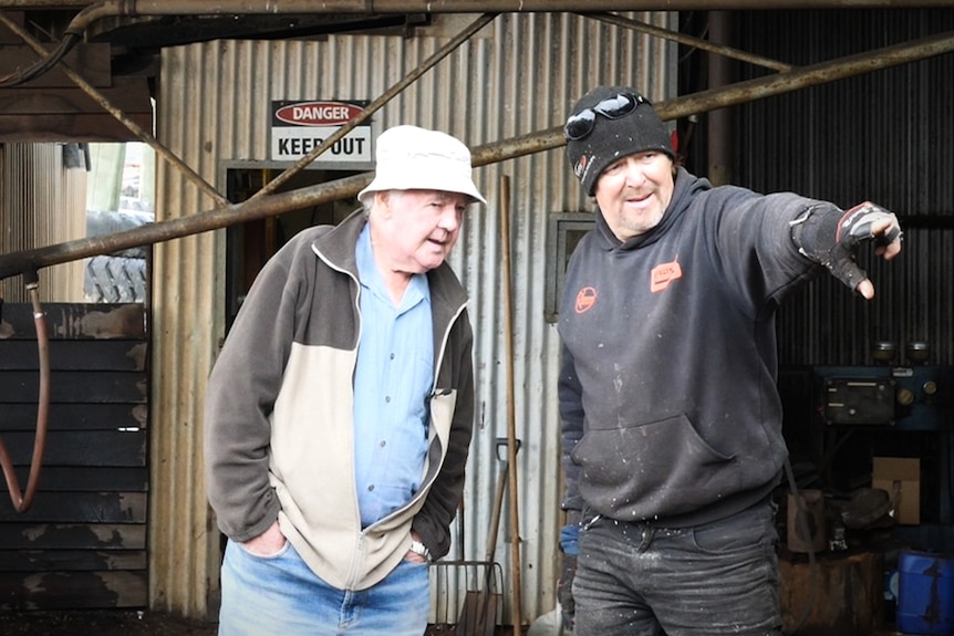 An older man chats with a younger man at a timber mill