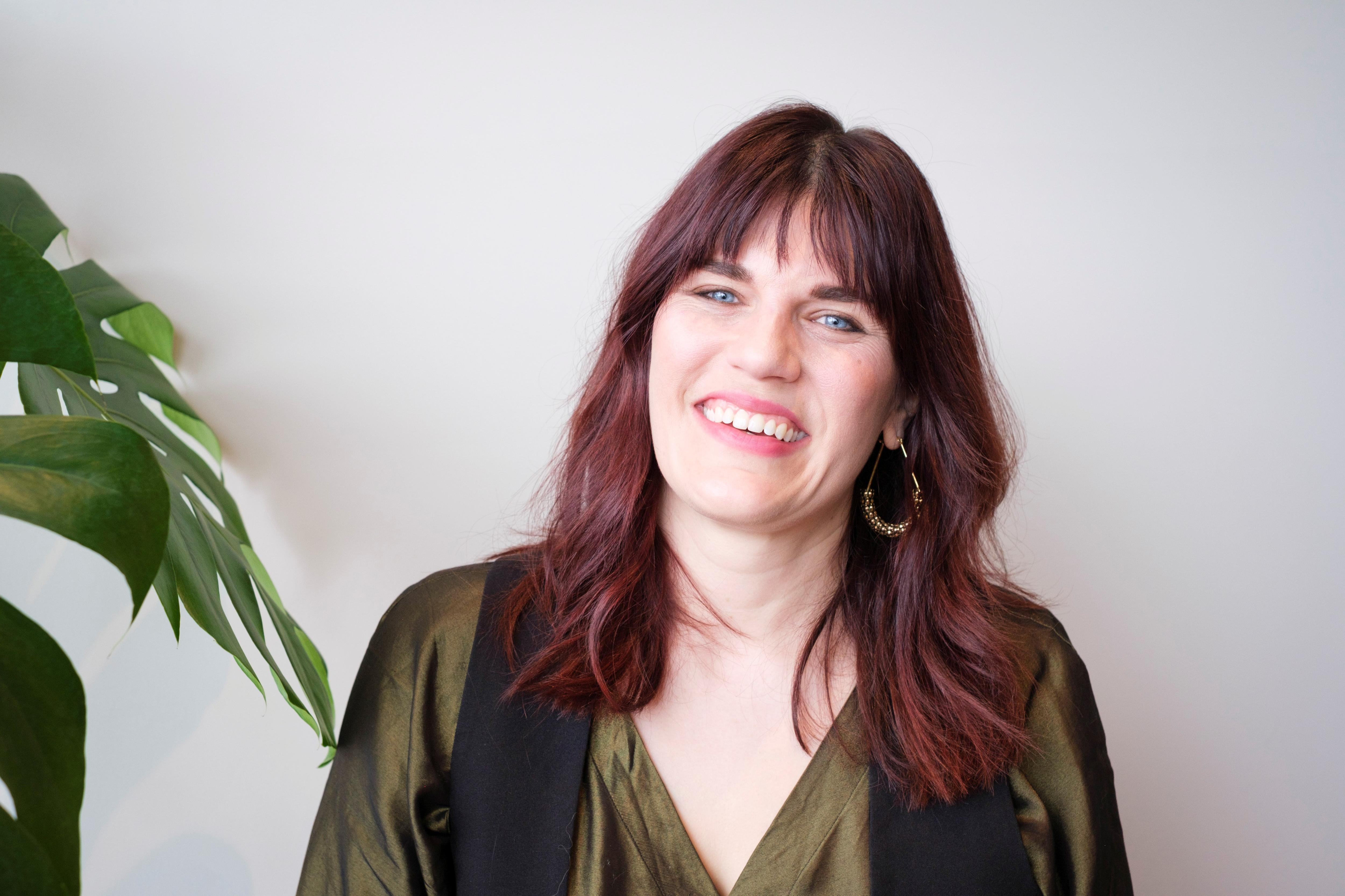 A professional headshot of Dr Sarah Ashton smiling widely in a green silky blouse.