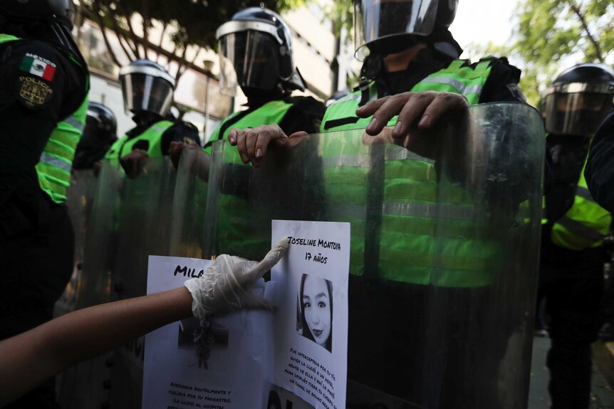 a demonstrator sticks a flyer of a women who was a victim of violence on the riot shield of police officer