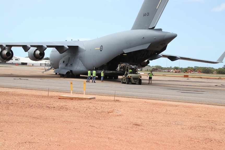 Crews unloading supplies from a large grey aircraft