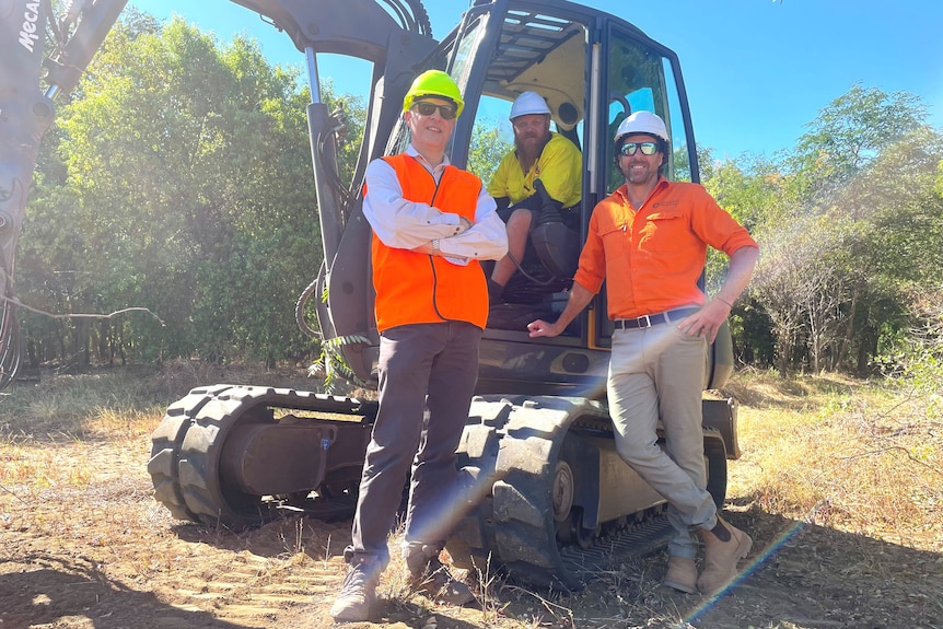 Three men with hard hats posing around a tree feller