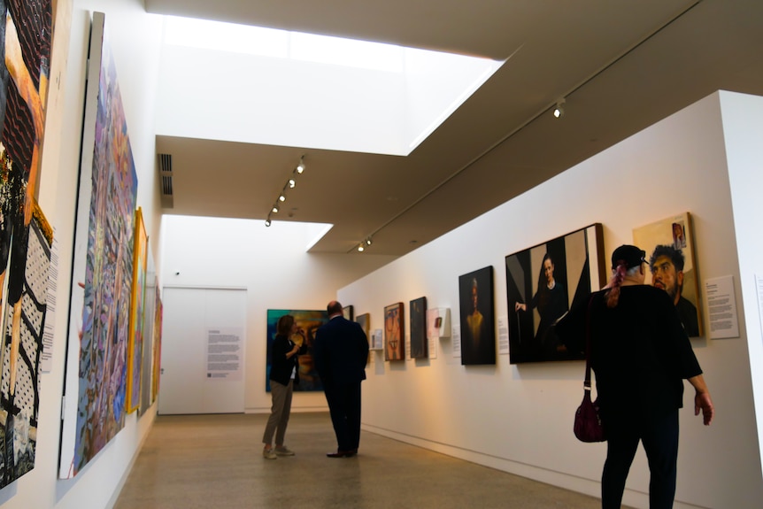 people observe works of art on the walk in a gallery with high ceilings