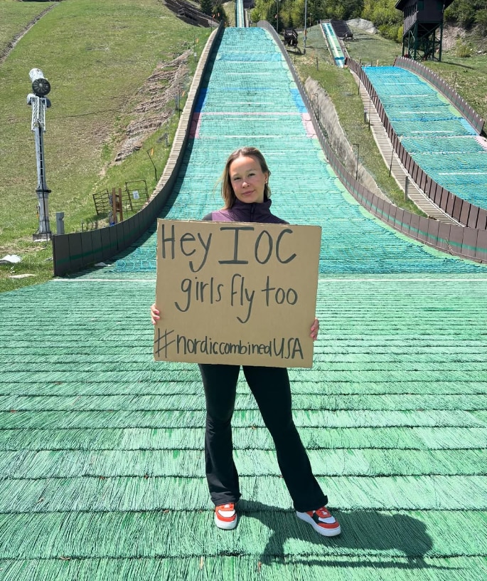 Annika Malacinski holds a sign at the base of a ski jump