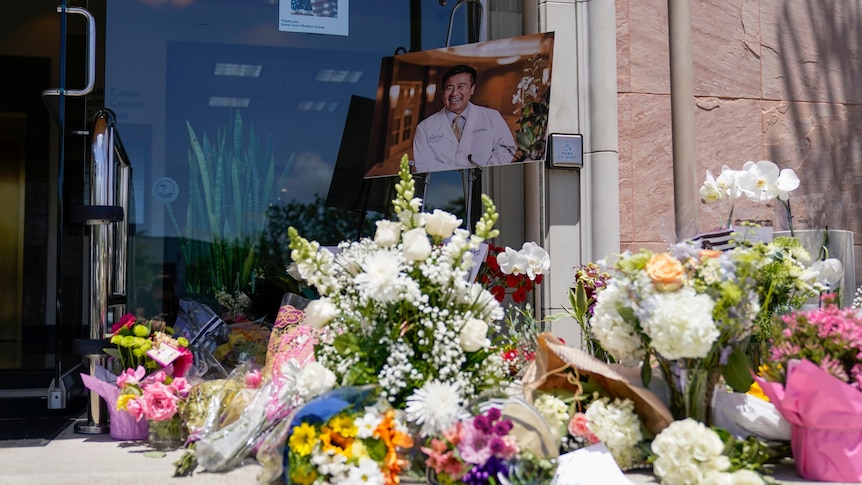 A variety of flowers and a portrait of a victim of gun violence make up a street memorial outside an office building