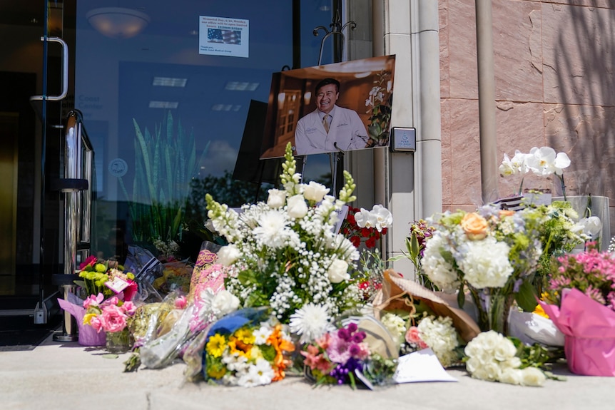 A variety of flowers and a portrait of a victim of gun violence make up a street memorial outside an office building