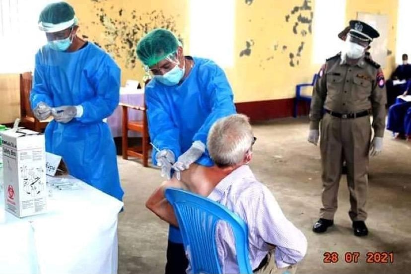 A man sits in a chair while men in scrubs prepare a needle to put into his arm.