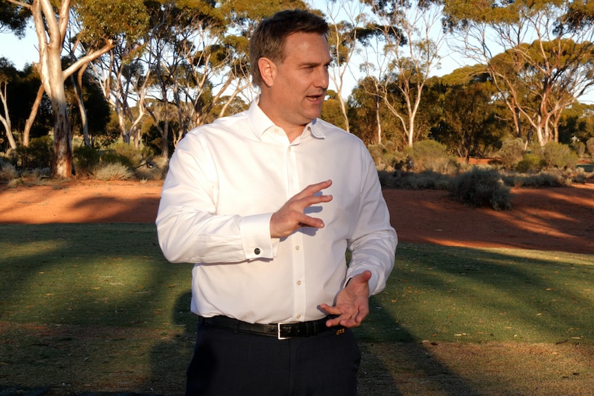 A man wearing a white shirt gestures as he talks.