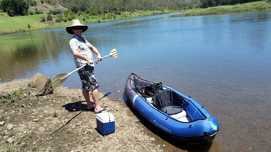 Quentin Smith smiles as he stands besides an unknown river with a canoe and paddle