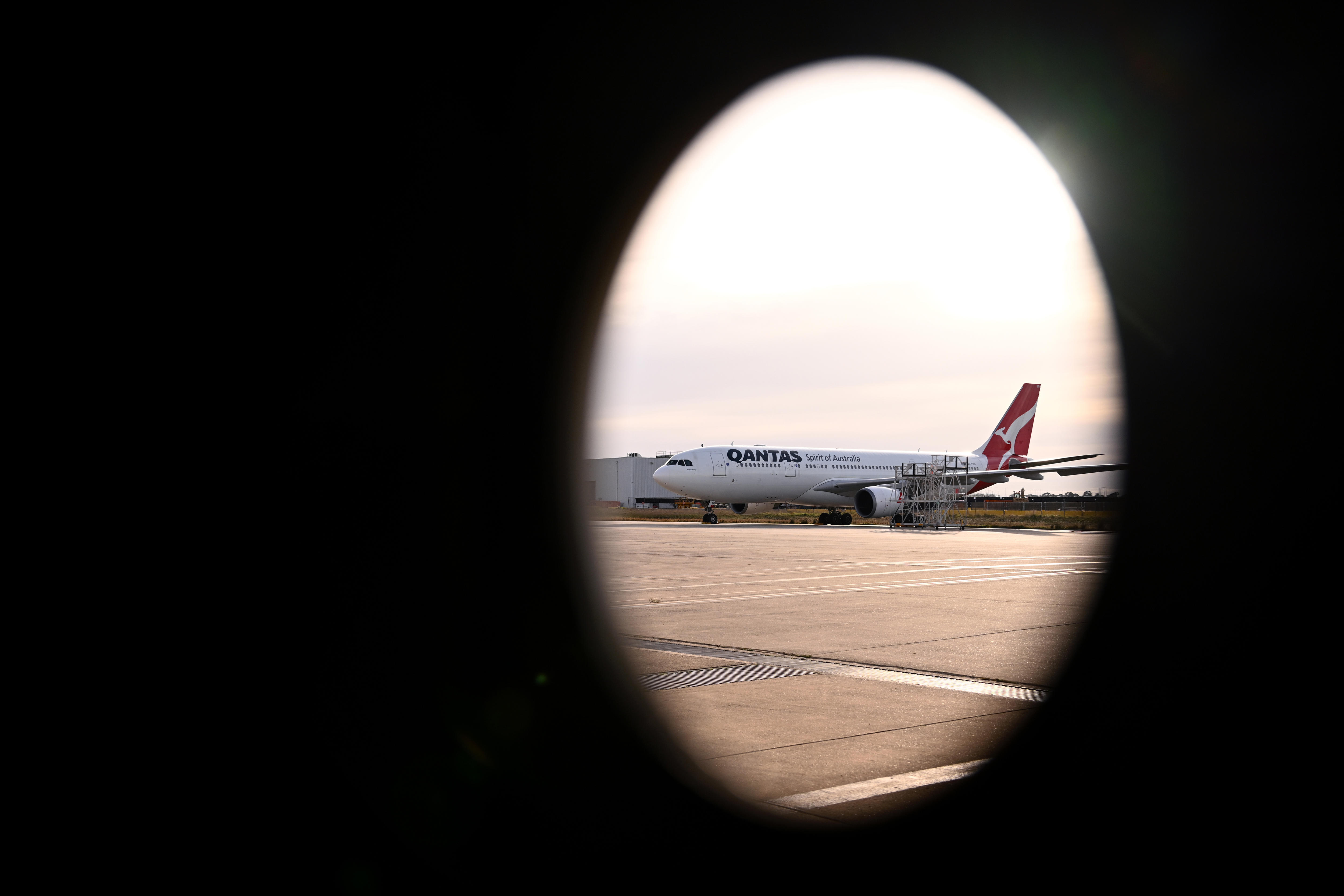 A Qantas aircraft is seen on the tarmac through a circular window. 