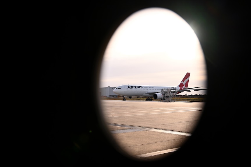 A Qantas aircraft is seen on the tarmac through a circular window. 