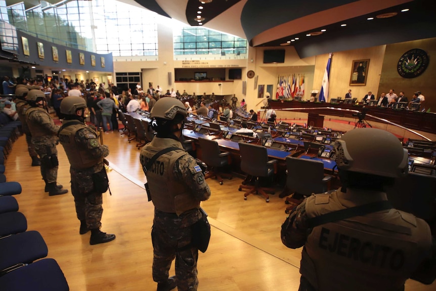 Soldiers wearing uniforms and carrying guns stand at back of a Congress hall.