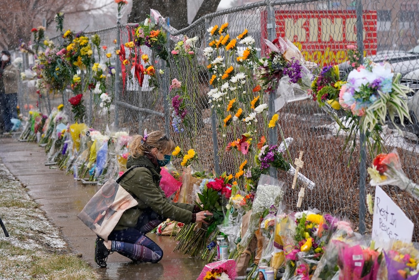 A mourner leaves a bouquet of flowers along a wire fence covered in flowers.