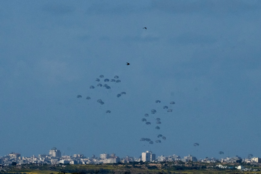 Wide shot of dozens of parachutes dropping supplies into Gaza.