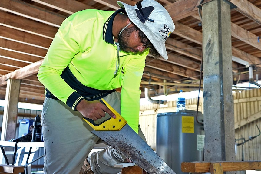 Young man cutting timber with a hand saw