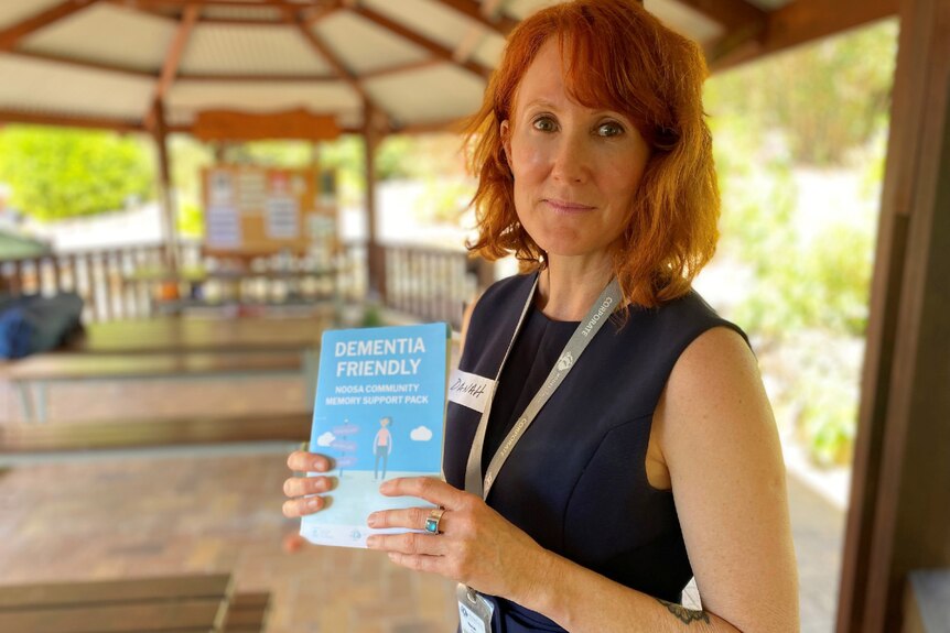 Woman stands under a rotunda holding a brochure that says Dementia Friendly