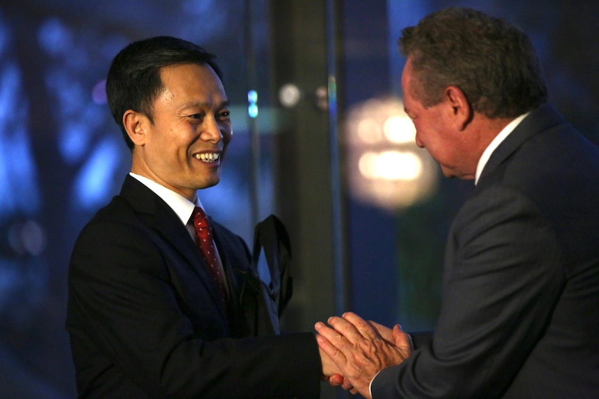 A man wearing a suit and smiling shakes hands with another man, Andrew Forrest.