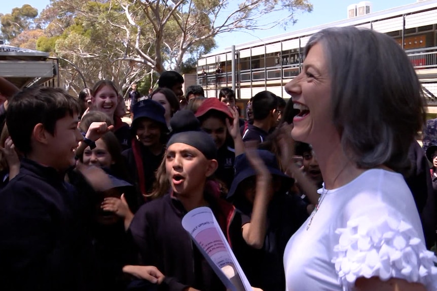 A woman wearing a white top laughs with children behind