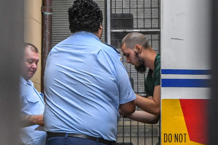 A man is lead out of a corrections van by uniformed officers