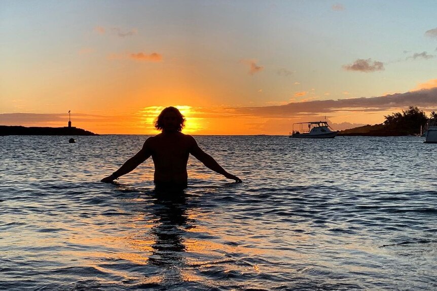 A man with shaggy hair in the water at sunset 