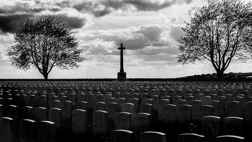 Black and white photo of a war cemetery with a central cross flanked by two trees.