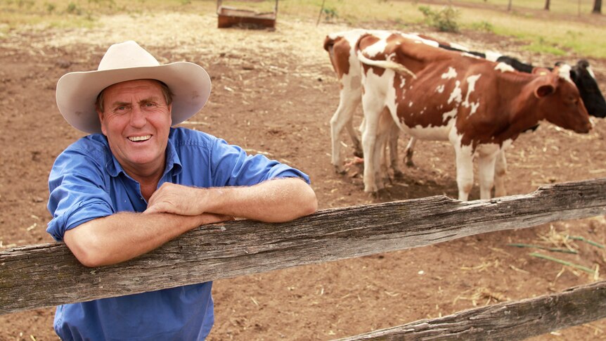 A farmer leaning against a cow pen fence and smiling.