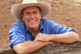 A farmer leaning against a cow pen fence and smiling.