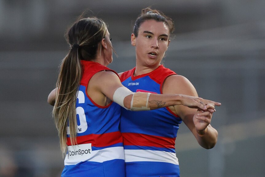 Two Western Bulldogs AFLW players embrace and catch their breath after a goal.