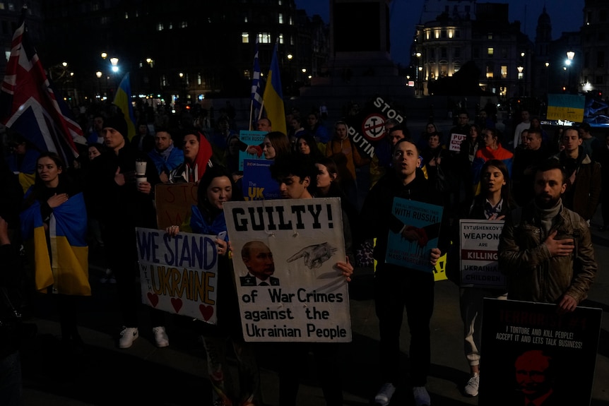 A group of people hold various placards at night time.