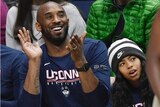 Kobe Byrant claps in a blue shirt while sitting in the crowd with his daughter Gianna wearing a beanie
