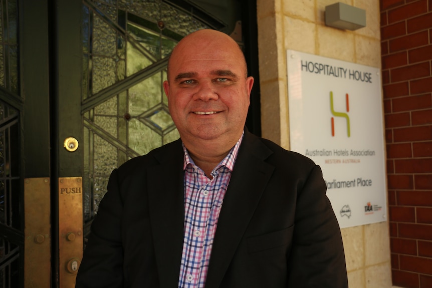 Mr Woods smiles in front of a glass door and sign saying "hospitality house".