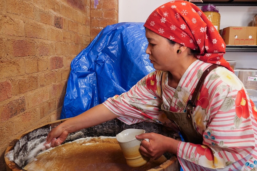 Woman in traditional Japanese clothing sprinkling salt on barrel of miso