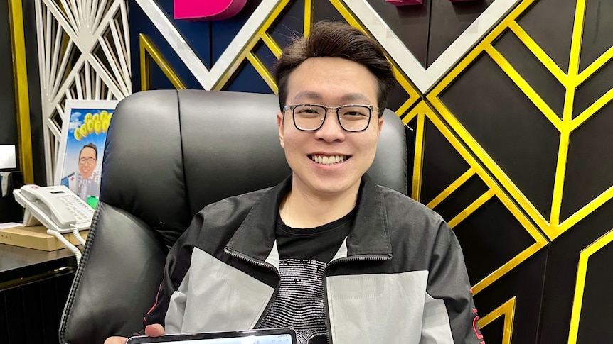 Man wearing glasses holding a laptop smiling to camera.