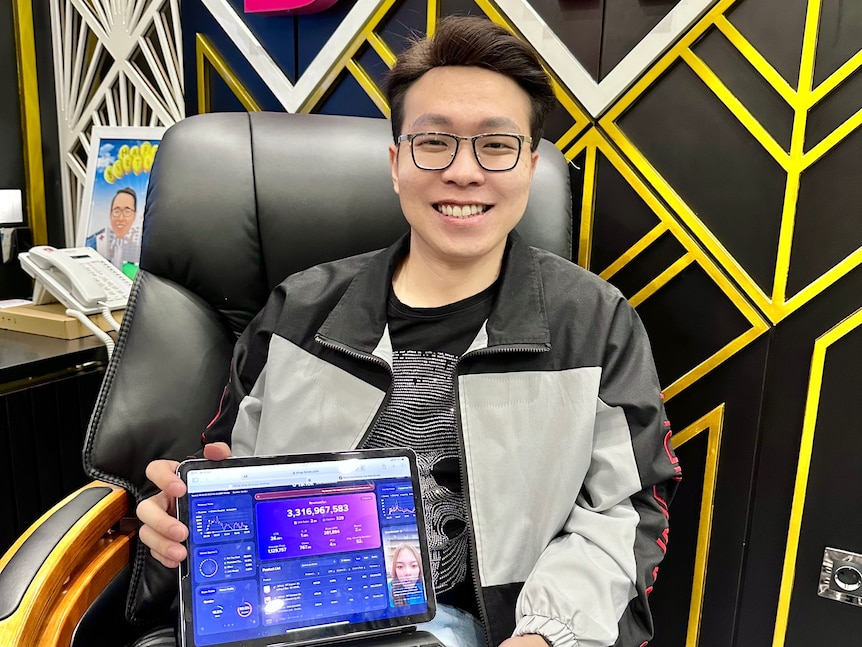 Man wearing glasses holding a laptop smiling to camera.