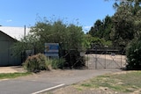 Exterior of a building, fence and sign with trees surrounding site