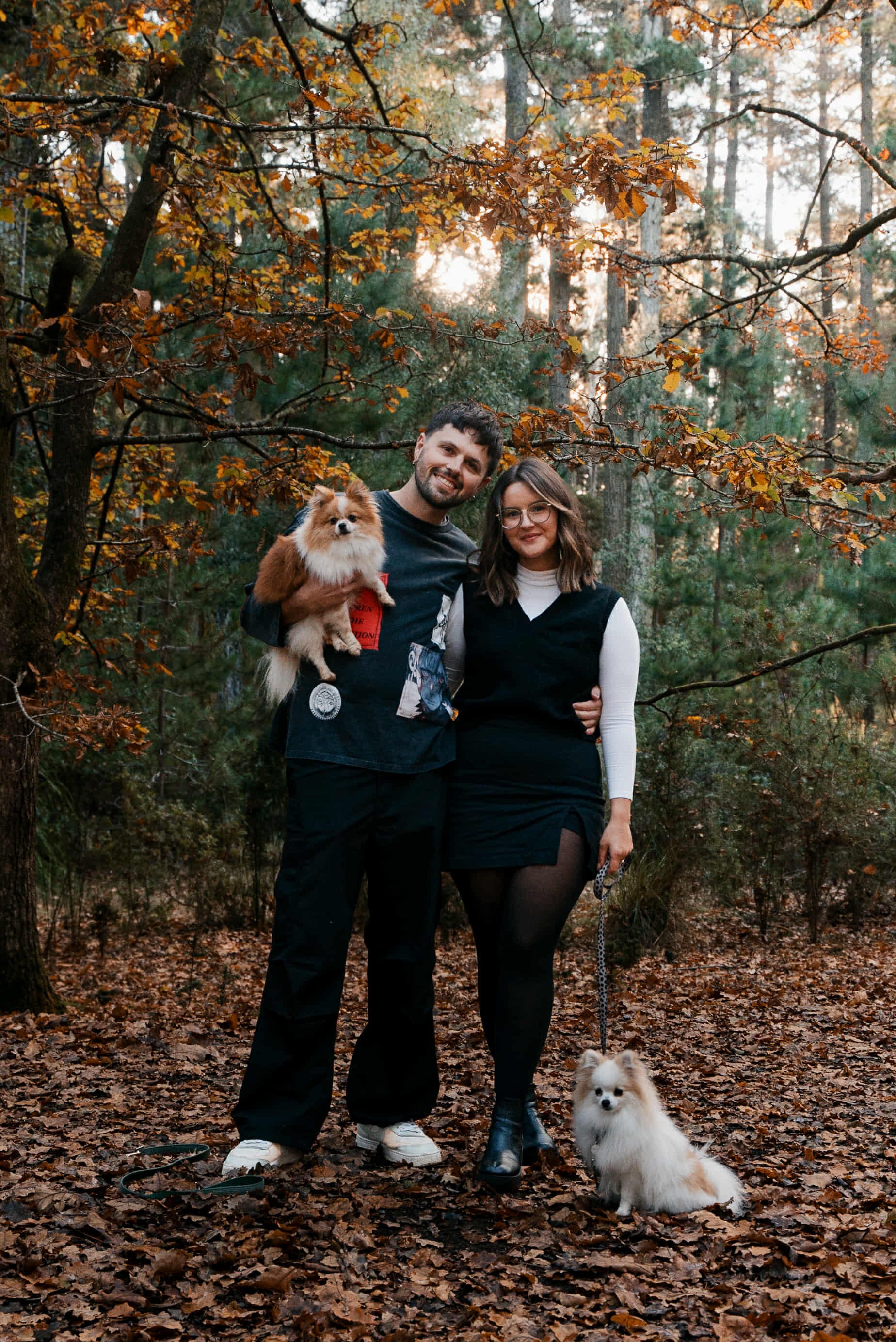 um casal em pé nas folhas de outono com um cachorro corgi.