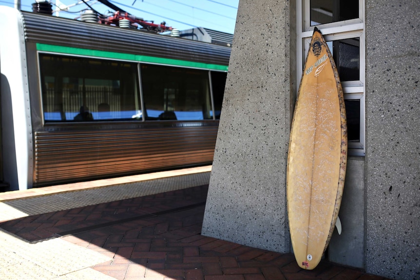 An abandoned surfboard at a Perth train station, with a train in the background.