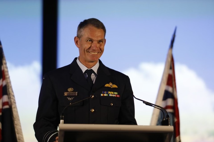 Rob Chipman, wearing his uniform with air force badges smiling behind a podium