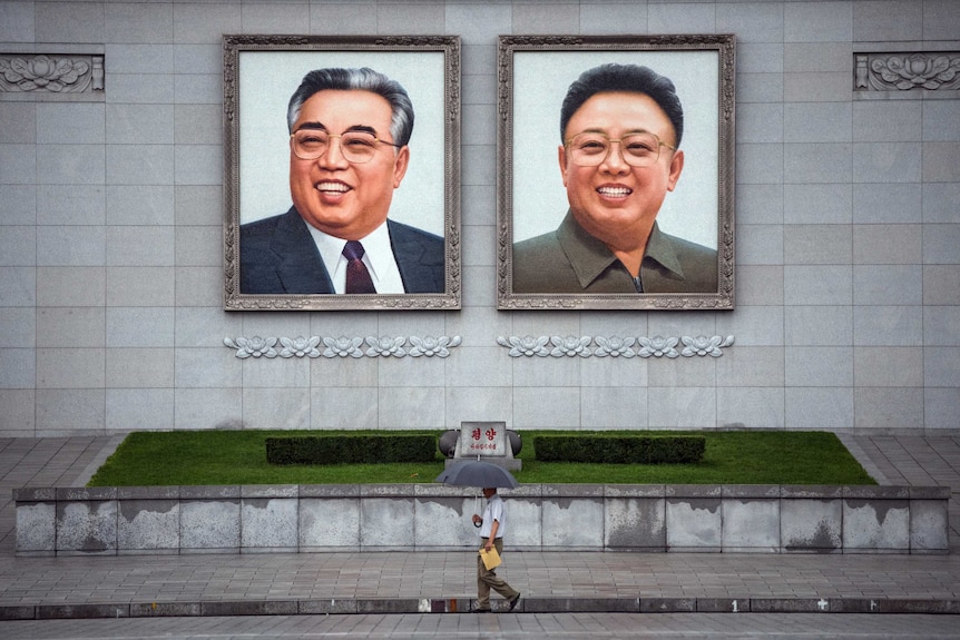 People walk beneath huge pictures Pyongyang